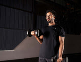 Male athlete in a gym doing bicep curls using two dumbbells, wearing a black activewear tee.