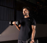 Male athlete in a gym doing bicep curls using two dumbbells, wearing a black activewear tee.