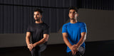 Two young male athletes kneeling in a gym setting wearing blue and black activewear t-shirts. 