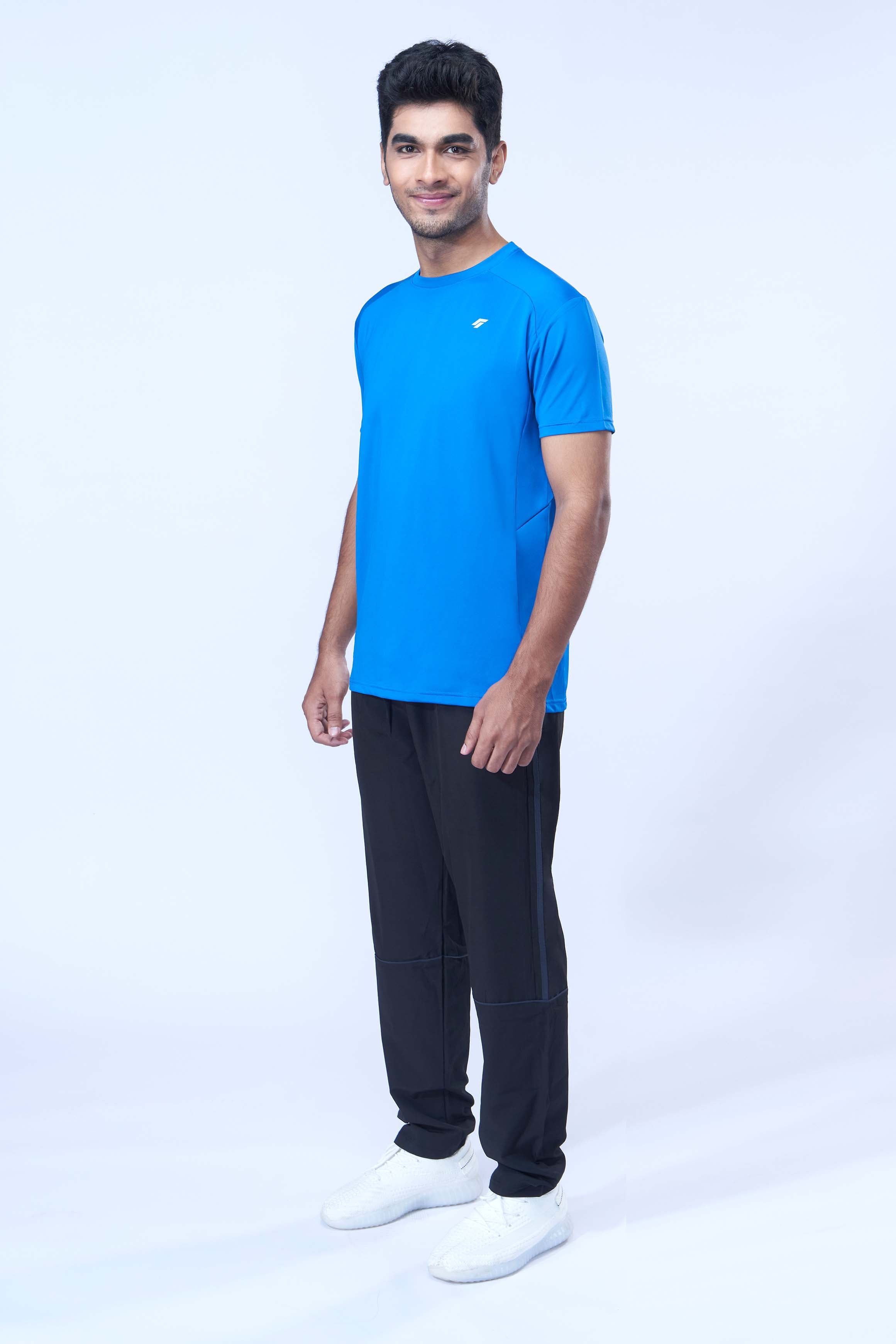 Man posing in a sustainable blue activewear t-shirt and joggers in front of a white wall.