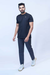 Man posing in a sporty black activewear t-shirt and joggers in front of a white wall.