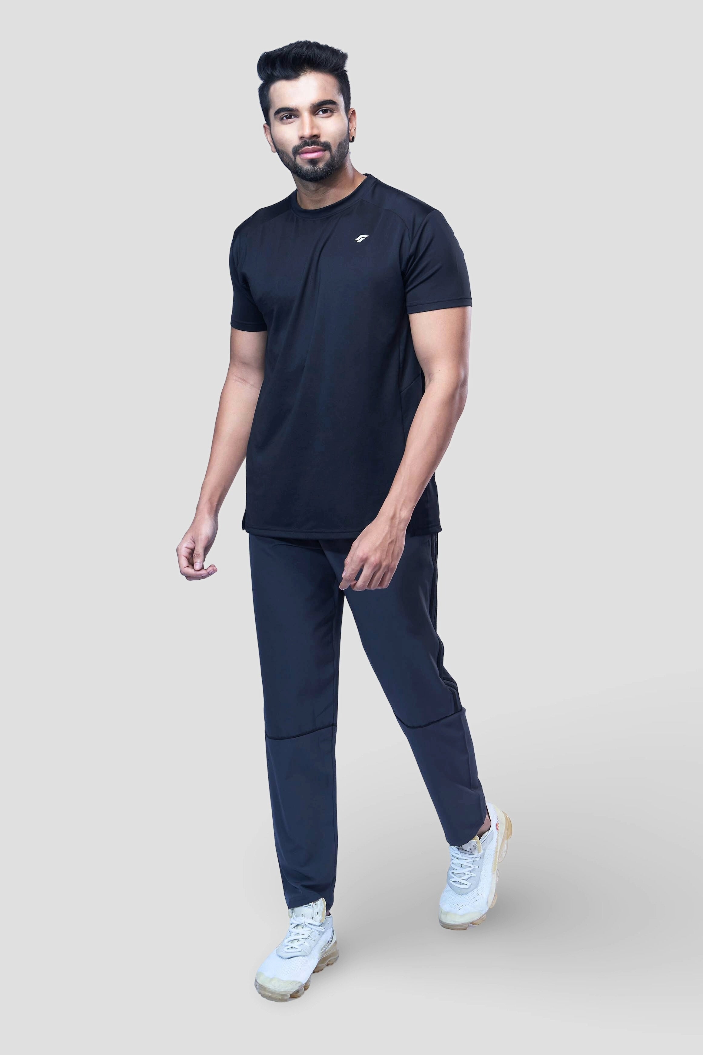 Man posing in a sporty black activewear t-shirt and joggers in front of a gray wall.