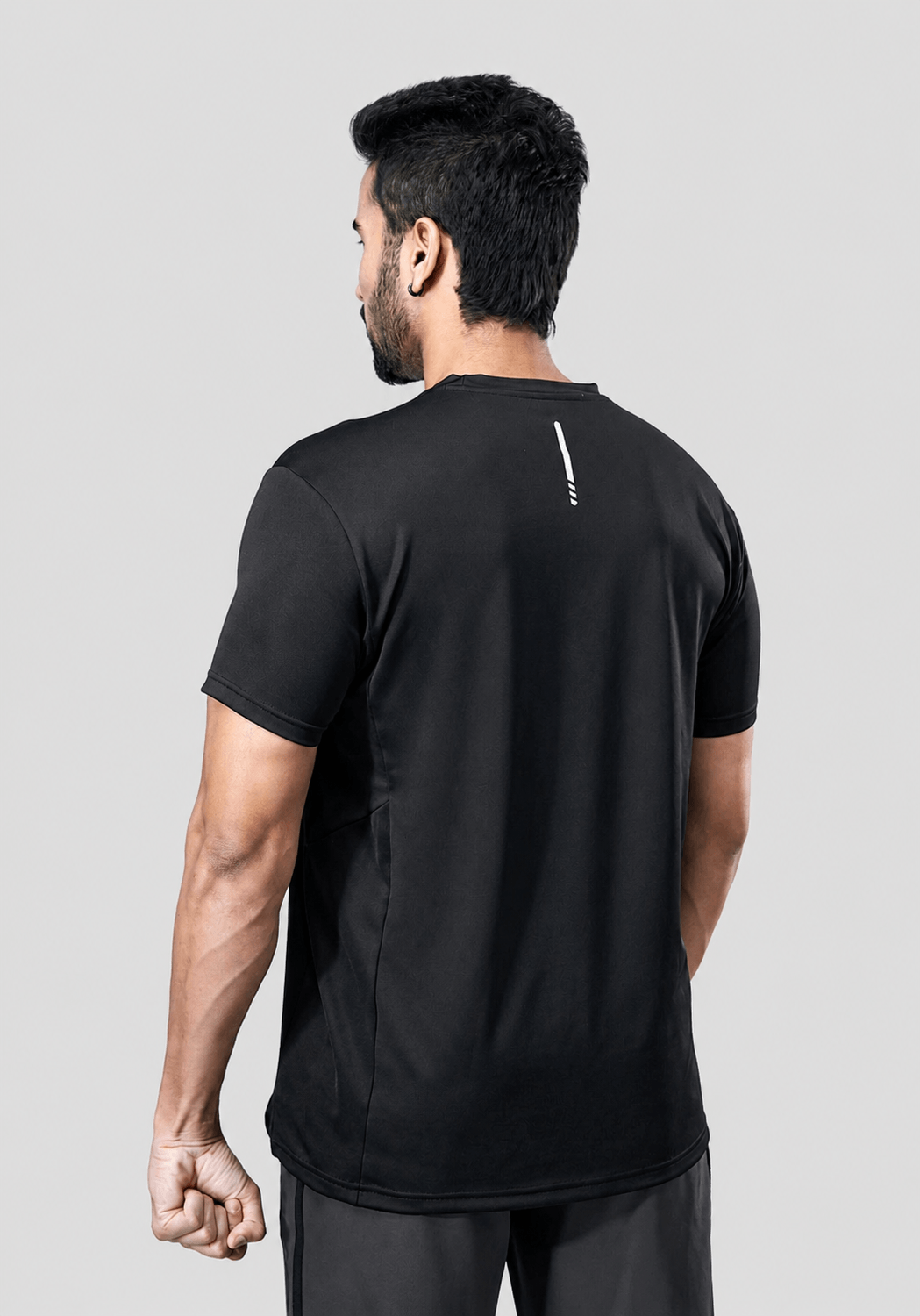 Back view of a man wearing a recycled polyester black activewear t-shirt against a gray background.